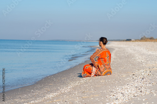 Woman in ethnic dress relaxes and meditates on a deserted beach