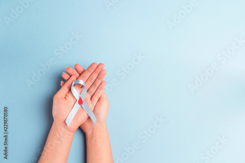 Helping hands holding blue ribbon awareness with red blood drop on a blue background. World diabetes day,14 november. photo