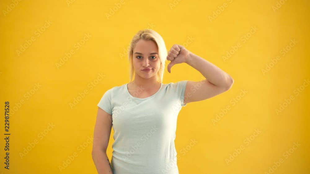 Young blond plus size model showing thumbs down gesture isolated at yellow background Young blond plus size model showing thumbs down gesture isolated at yellow background