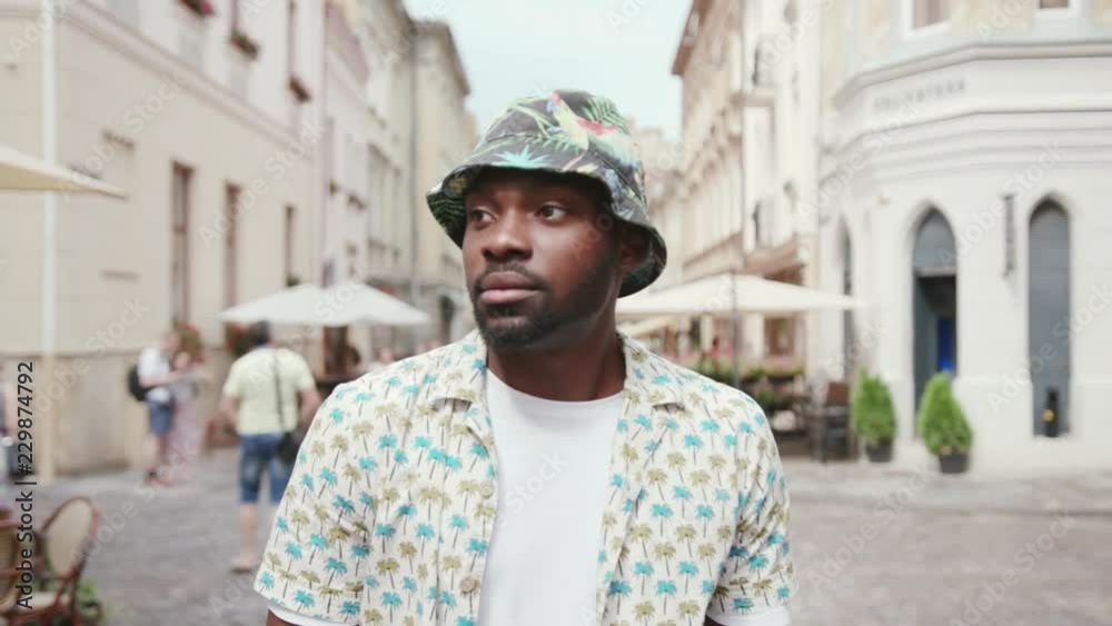 Likable African guy wearing Panama hat walking down the street, tourning around. Serious terrific young man looking right. City. Daytime. Likable African guy wearing Panama hat walking down the street, tourning around. Serious terrific young man looking right. City. Daytime.