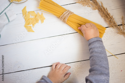 little baby's hands holding pasta on the white wooden table, cooking with children concept