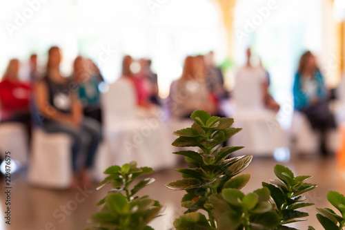 Group of people listening to a conference in an alternative health center, as seen from behind a green shrub - Closeup picture with blurry people in the background photo