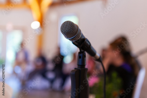 Microphone on a straight stand, with blurry specialists giving a conference in the background - Closeup picture on the vocal microphone photo