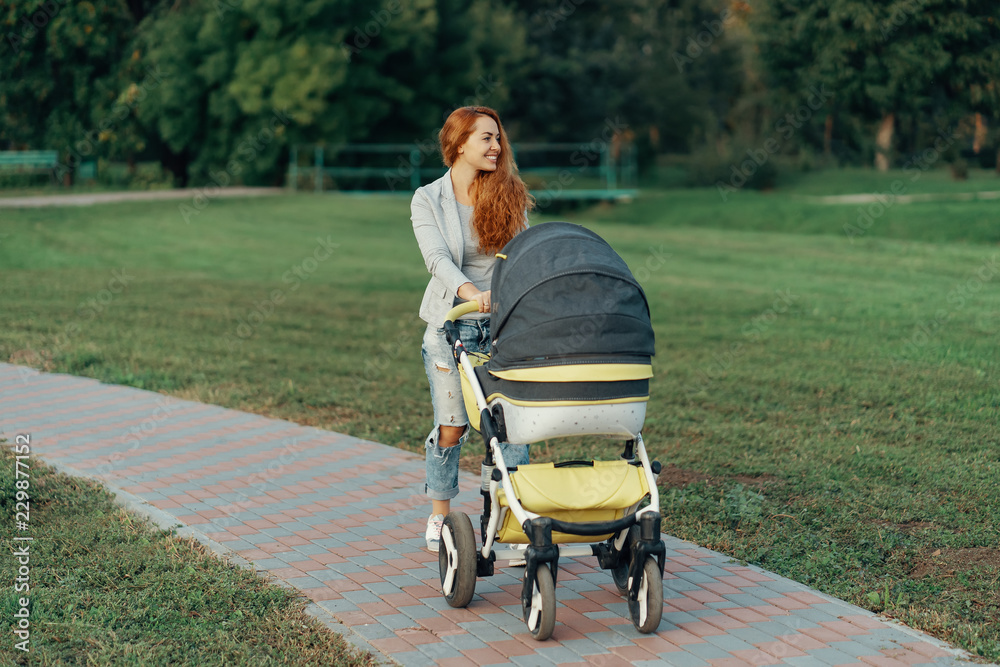 Mother enjoying walk carrying her little child in his baby troll Mother enjoying walk carrying her little child in his baby troll