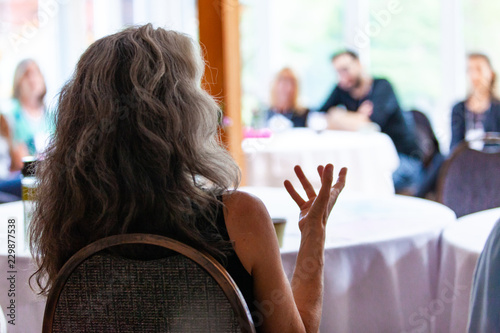 Woman is explaining her position in a convincing speech in front of a blurry group of very interested people - Pictured from the back in an alternative health center photo