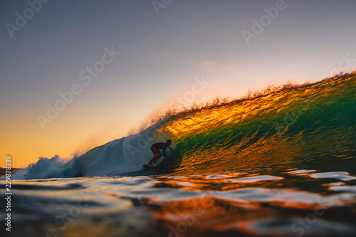 Fototapeta Naklejka Na Ścianę i Meble -  Surfer ride on barrel wave at warm sunset. Professional surfing in ocean, Bingin beach