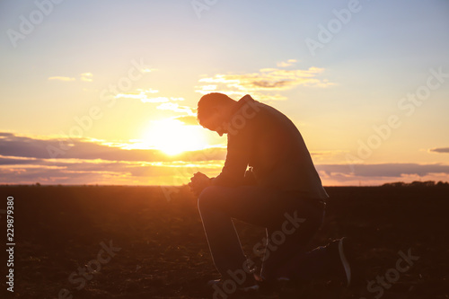 Religious man praying outdoors at sunset