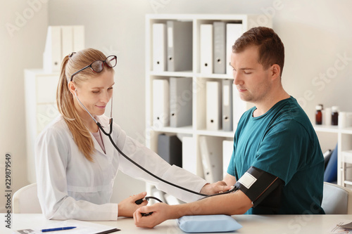 Obraz na plátně Female doctor measuring blood pressure of male patient in hospital