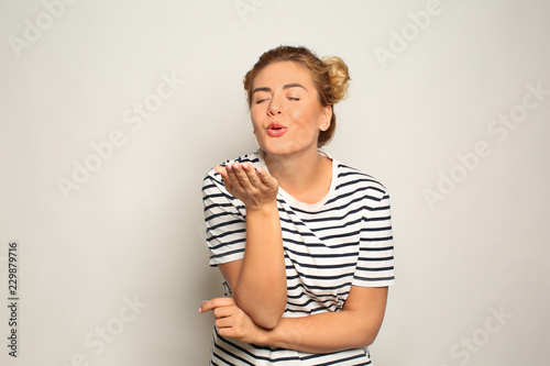 Portrait of beautiful young woman blowing kiss on light background