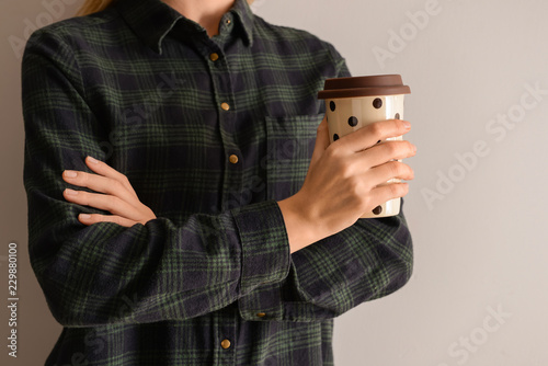 Woman holding coffee cup on light background, closeup photo