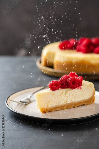 Slice of New York Cheesecake with raspberries on a dark background.