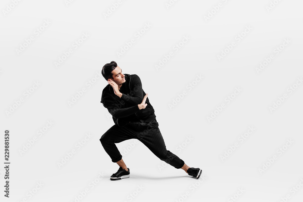Handsome dancer dressed in a stylish black clothes is dancing street dance. He makes stylized movements with his hands