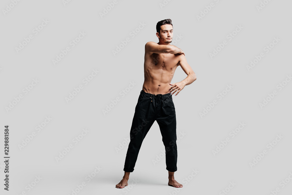 Dark-haired handsome young dancer with  bare torso wearing a black pants makes dancing movements on a white background