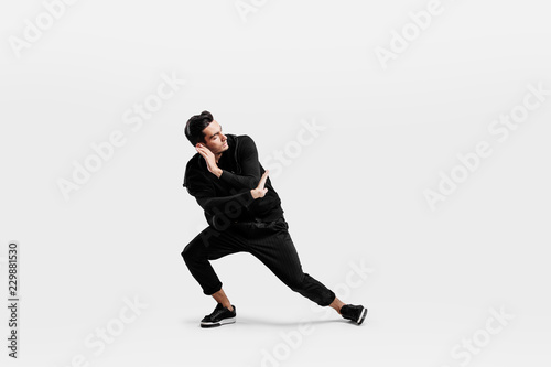 Handsome dancer dressed in a stylish black clothes is dancing street dance. He makes stylized movements with his hands