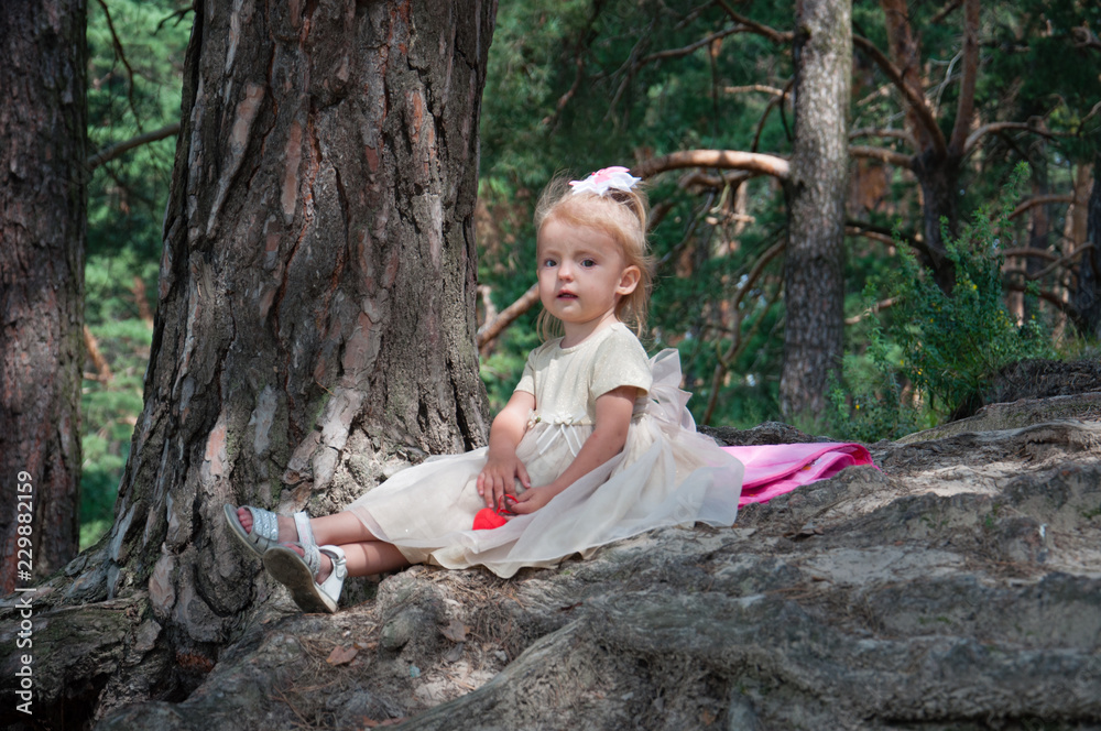 Little beautiful girl playing in nature in the forest. Sits on a fork with a red heart in his hands Little beautiful girl playing in nature in the forest. Sits on a fork with a red heart in his hands