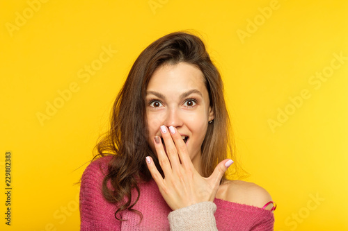 surprised shocked astonished amazed girl covering mouth with hand. unbelievable news. young beautiful woman on yellow background. emotional reaction concept.