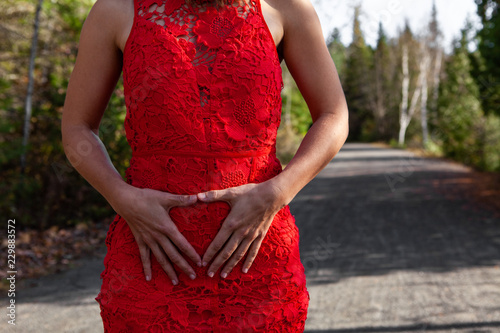Young woman in a red dress is doing an ovary related empowerment symbol around her belly button while on a walking path - Closeup picture taken on a very sunny autumn day