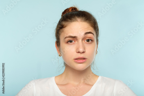 bewildered dubious distrustful girl with raised eyebrow. young beautiful woman with a hair bun on blue background. emotional facial expression.