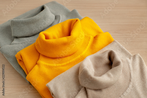 Three turtlenecks of different colors. Three turtleneck classic style for the autumn and winter seasons. Warm clothing from knitwear on a wooden background. Women's fashion.