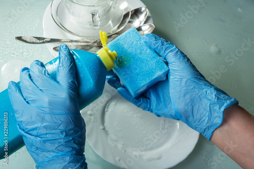 Hands in blue gloves wash the dishes. Sponge for washing and means of fat