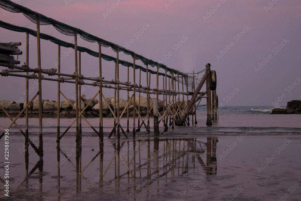 Peaceful evening on the shore, with scenic pink sunset reflected on water ant metallic pier; adriatic sea