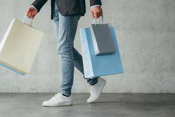 shopping therapy for males. casual guy walking holding lots of bags with goods.