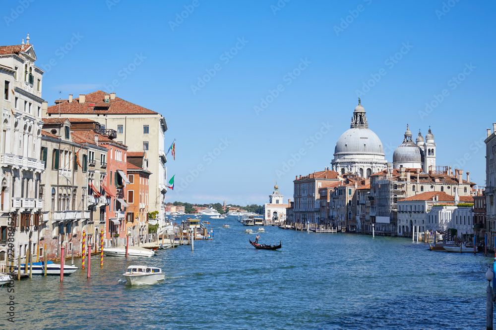 Grand Canal in Venice with gondola and Santa Maria della Salute basilica in Italy, blue sky