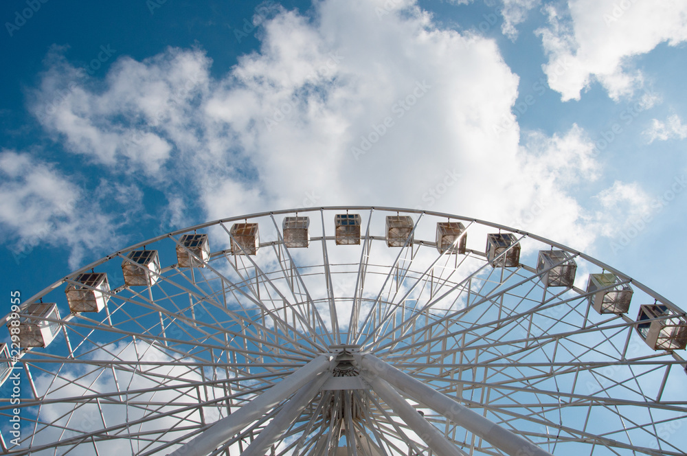 Ferris wheel in an amusement park, view from below look upwards. Sky background with clouds with place for text.