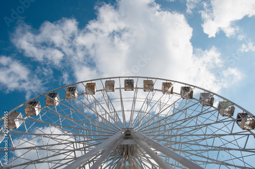 Ferris wheel in an amusement park, view from below look upwards. Sky background with clouds with place for text.