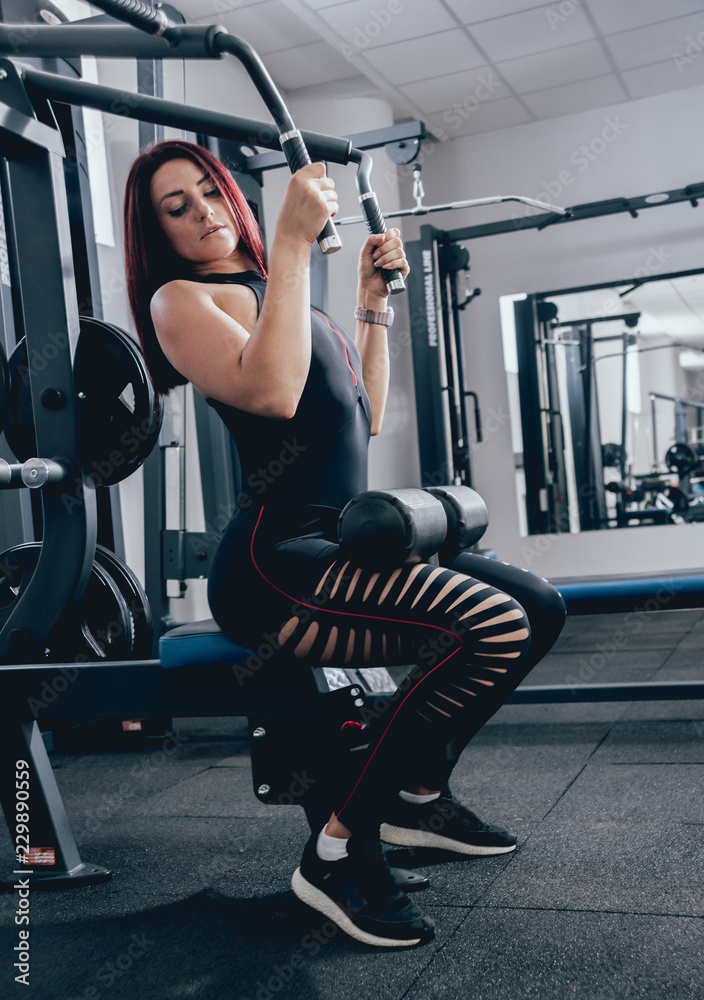 Fototapeta premium Beautiful athletic young woman making exercise at the gym. Young woman with muscular body.