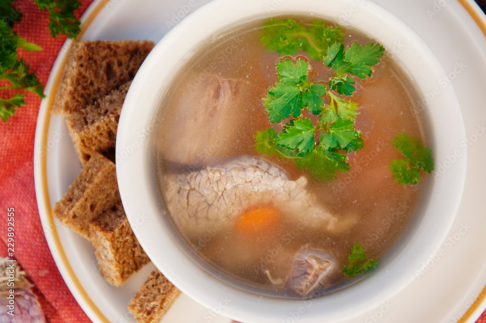 Clear beef broth, bouillon in white bowl and vegetables on wooden table. Rustic style. Top view. Clear beef broth, bouillon in white bowl and vegetables on wooden table. Rustic style. Top view.