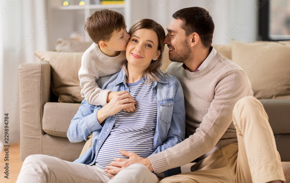 pregnancy, people and family concept - happy pregnant mother, father and little son hugging on sofa at home pregnancy, people and family concept - happy pregnant mother, father and little son hugging on sofa at home