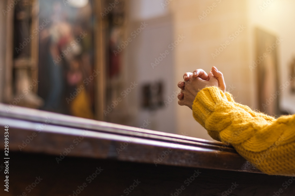 Christian woman is praying with hands crossed in church  - obrazy, fototapety, plakaty 