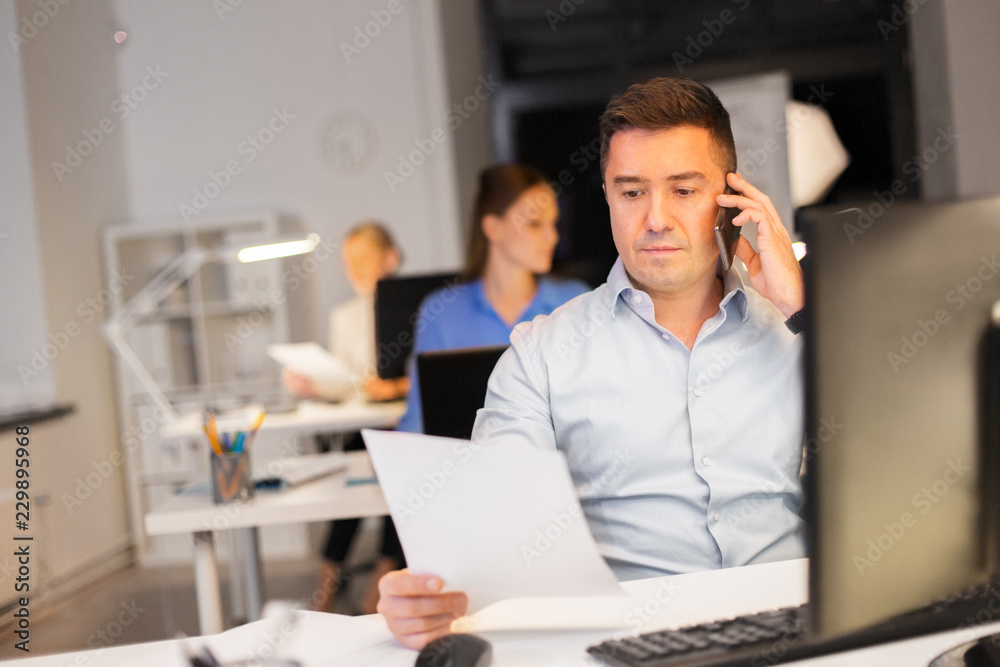 business, deadline and technology concept - man with computer calling on smartphone late at night office business, deadline and technology concept - man with computer calling on smartphone late at night office