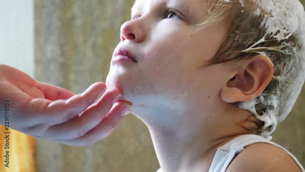 Young mother shaves head of blond boy with razor for preventing pediculosis. Good family tradition. Child is happy from hygiene procedures.