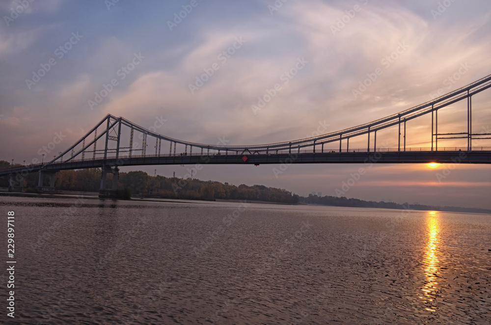 Wide angle landscape panorama of Dnipro River, embankment and Pedestrian Bridge. Colorful vibrant sky, sun reflected in the water. Foggy autumn morning during sunrise. Kyiv, Ukraine