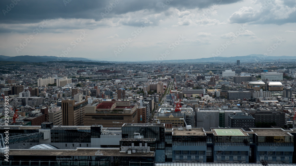Aerial shots of the city of Kyoto. Skyscrapers and buildings expand out into the distance of the Japanese city as a stormy sky and clouds form over the cityscape.