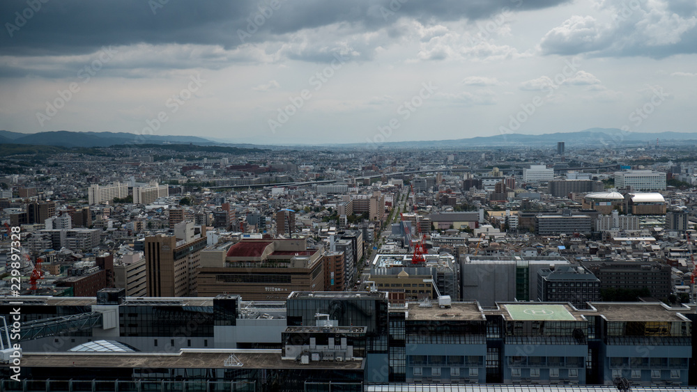 Obraz premium Aerial shots of the city of Kyoto. Skyscrapers and buildings expand out into the distance of the Japanese city as a stormy sky and clouds form over the cityscape.