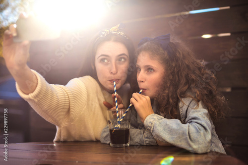 Mother and daughter taking a selfie while drinking from the same glass
