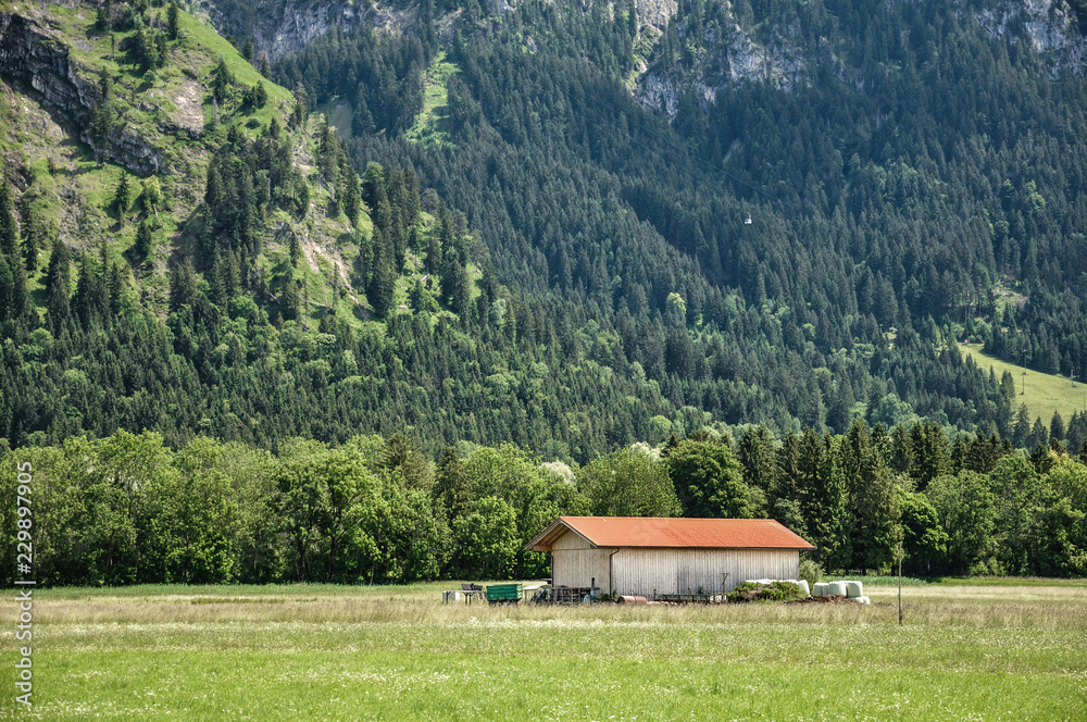 An old bavarian farm in Bavarian Alps, south Bavaria, Germany. Spring or summer sunny day. Mountains on a background. Typical peaceful bavarian landscape.