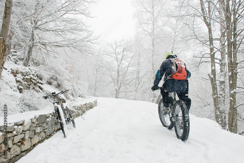 man riding with electric bicycle, e-bike, ebike, pedal on snowy road, during snow storm, blizzard, high mountain, end of winter, spring, cold, alps, adventure, Piedmont, Italy