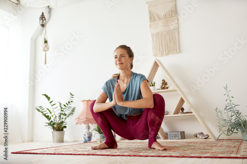 fitness, people and healthy lifestyle concept - young woman doing garland pose at yoga studio photo