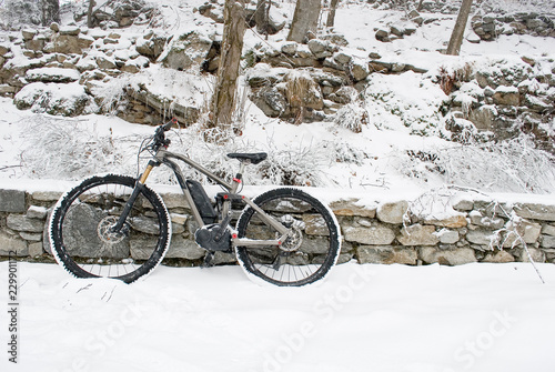 electric bicycle, e-bike, ebike, resting on a wall of rocks, snowy road, mountain forest during snowstorm, sports, end of winter, handlebars, wheel, display, cold, alps, Piedmont, Italy