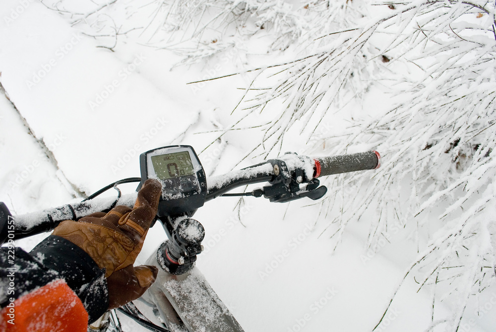 detail of handlebars of electric bicycle, e-bike, ebike, a man's hand on display, mountain forest during snow storm, blizzard, sport, end of winter, cold, alps, adventure, Piedmont, Italy