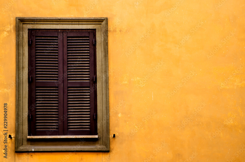 A wooden window on the bright orange wall of one of the houses of Rome. Italy
