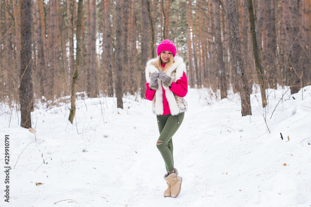 Beauty, nature and people concept - beautiful blond woman walking in pink hat and sweaters in winter wood and smiling Beauty, nature and people concept - beautiful blond woman walking in pink hat and sweaters in winter wood and smiling