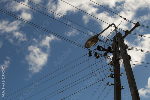 Electric wires hanging on a pole with a lighting lamp photographed from below on a background of blue sky with white clouds