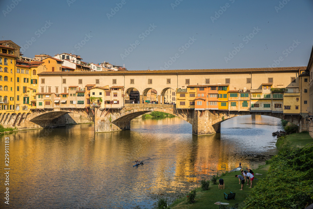 Yoga on the banks of the river Arno, while a kayak paddles under the Ponte Vecchio in Florence