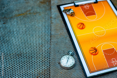 Clipboard with basketball field, coach whistle and stopwatch on steel net background. Close up sport mockup template.