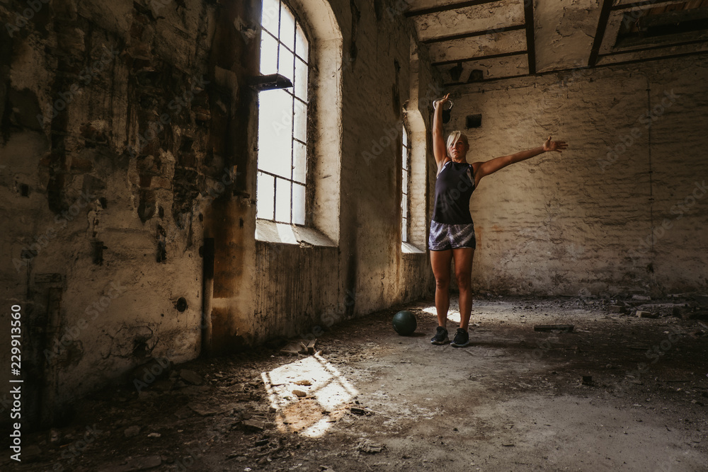 Athletic woman holding kettlebell up in an old building